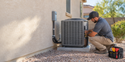 HVAC technician installing an outdoor air conditioning unit beside a stucco home in Arizona.